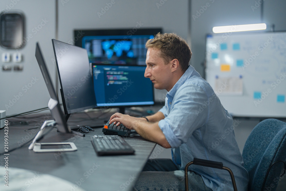 Fototapeta premium DevOps engineer, Caucasian male programmer working on computer monitors in modern IT office, software operations, system deployment, cloud infrastructure and advanced technology business innovation