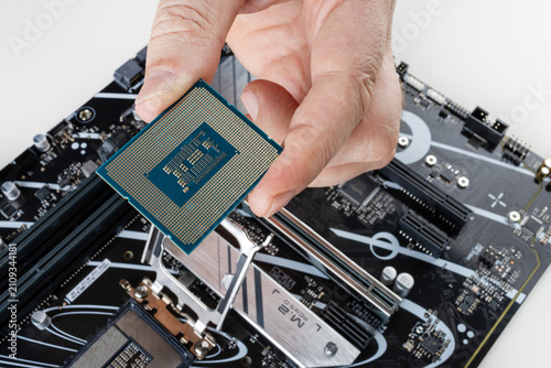 Close-up of a man holding a brand-new computer processor in his hand, with a motherboard visible in the background, highlighting technology, hardware installation, and PC building.