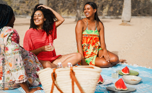 Happy multiracial girls eating watermelon and drinking fresh homemade lemonade while doing picnic on the beach - Summer and vacation concept - Main focus on center girl face - UGC content