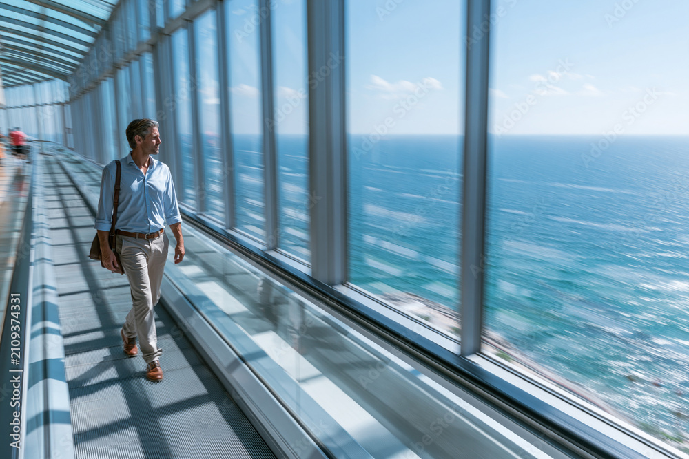 Obraz premium Professional on an escalator with sea-view windows, summer coastal business concept