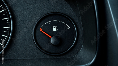 Close-up view of a vehicle's dashboard fuel gauge with a red indicator needle pointing near the empty mark on a dark textured console