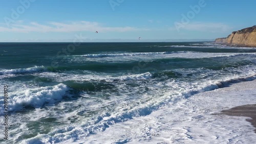 Midday aerial moving over waves to kitesurfers