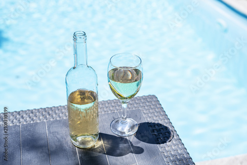 Bild auf Leinwand Glass and open bottle of white wine on concrete pool edge