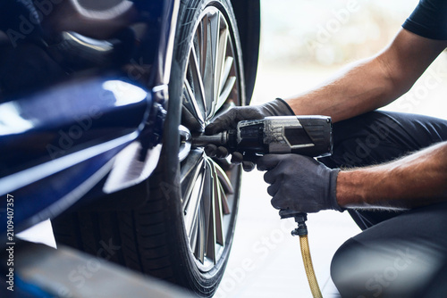 Mechanic using pneumatic wrench to change tyre in auto repair wo