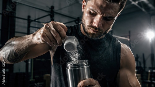 Athlete pouring supplement powder into steel shaker in gym