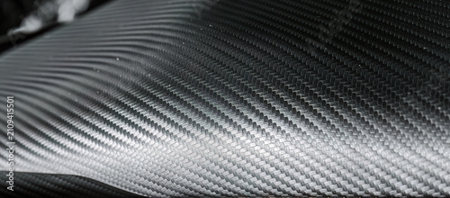 Close view of black carbon fiber style surface showing woven structure and reflective texture. Useful for automotive design, technology themes, engineering projects, and modern backgrounds.