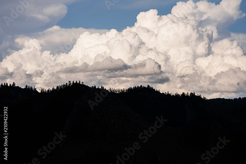 Canvastavla Majestic clouds dominate a blue sky above dark, forested mountains in central Mongolia, creating a striking silhouette against the bright backdrop