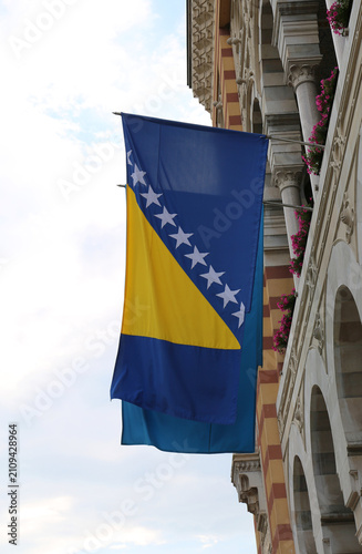 Quadro su tela Bosnian Flag  flying in the air  on Town Hall building with flowers in Sarajevo,