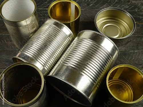 Different empty steel cans for storage of food are on a black wooden board, top view