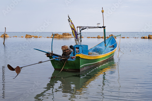 Traditional fishing boat resting on calm tropical waters near a small harbor. Image represents local fisheries, sustainable fishing practices and maritime transportation.