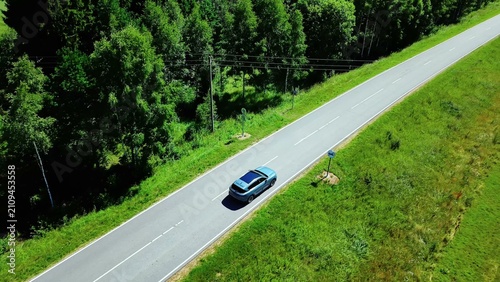 Car traveling along a scenic road bordered by vibrant greenery under bright sunlight