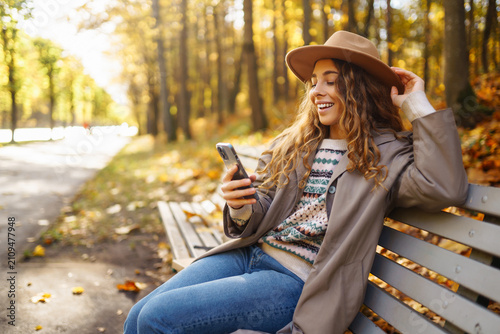 Cuadro en lienzo Woman sits on wooden bench, holding phone, surrounded by trees with yellow foliage