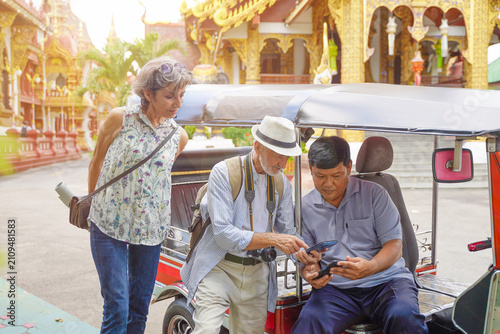 Konstfotografi American senior tourist uses his smartphone to pay for his tuk-tuk fare at his destination in Thailand