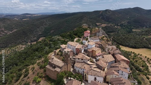 Flying low over houses of a scenic Spanish village in the Pyrenees, located on the top of a rocky mountain. 