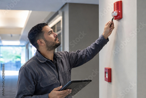 Male Inspector Testing Fire Alarm Device Building Corridor Tablet