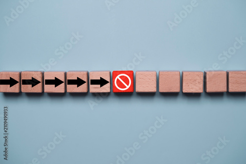 Wooden blocks with directional arrows stopped by a red prohibition symbol representing business obstacles  risk management  workflow interruption  compliance  restriction  and decision making.