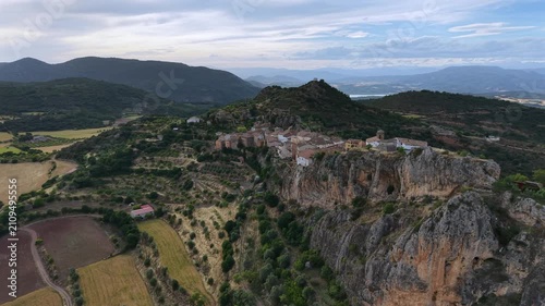 Aerial of a scenic Spanish village in the Pyrenees, located on the top of a rocky mountain. Dolly shot of village with typical olive groves and pastures in the valley below.