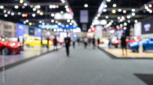Blurred motor show exhibition hall with crowd of people walking between colorful new cars under bright spotlights and bokeh lights creating professional automotive marketing background