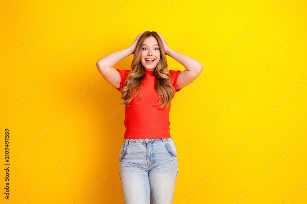 Fototapeta premium Happy surprised young woman in red shirt and jeans on bright yellow background expressing joy and excitement