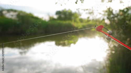 Fishing rod with bell alarm waiting for fish bite near quiet freshwater river. Concept of angling, patience and outdoor recreation