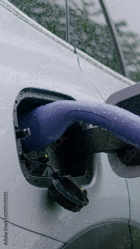 Electric vehicle charging process in the rain with a close-up view of the charging port and cable, showcasing the connection and water droplets on the surface