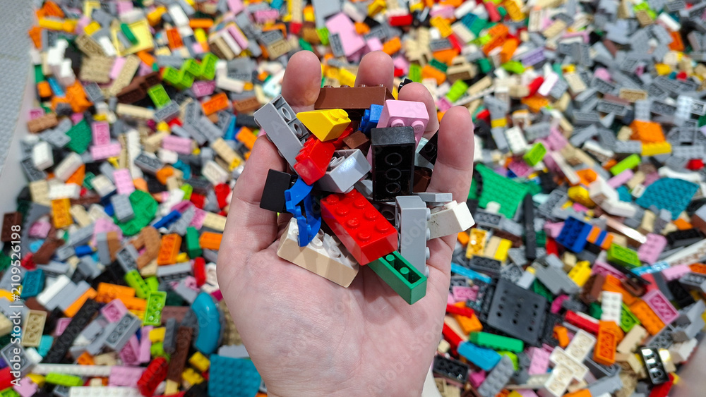 Fototapeta premium human hand holding colorful Lego blocks bricks above pile of unsorted toy pieces on June 18, 2026 in Bangkok, Thailand.