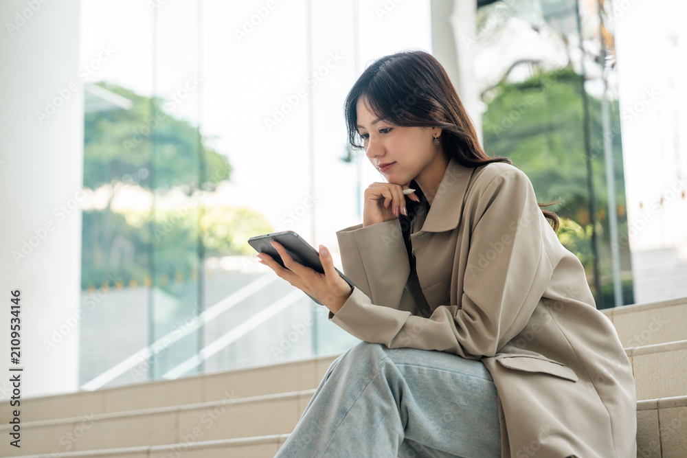 Obraz premium Cheerful young Asian businesswoman using digital tablet flexible working life balance in green urban park, modern lifestyle productivity remote work with digital online technology.
