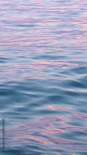 Soft sea waves ripple with pink sunset reflections vertical format, calm ocean water surface background, tranquil marine nature wallpaper