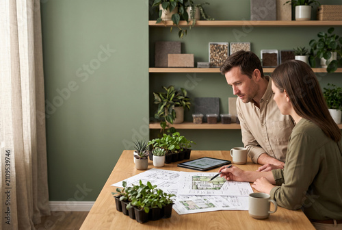 Couple planning home garden design. People working on landscape project with tablet and plans.