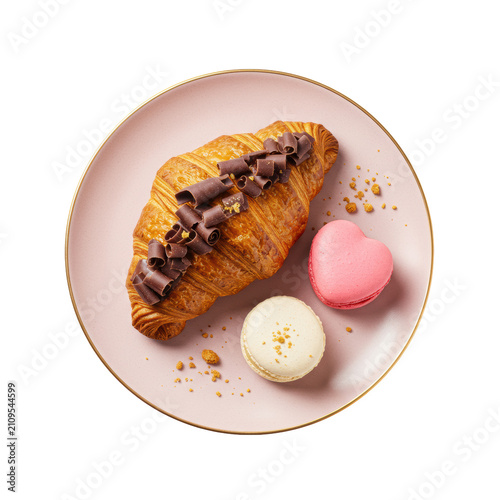 Golden-brown butter croissant with dark chocolate shavings, pink and off-white heart macarons on a speckled pink plate with gold rim, crumbs on a white background, romantic indulgence concept