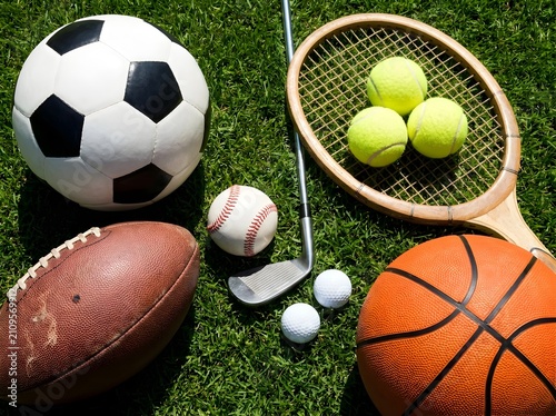 Various sports balls and equipment arranged on green grass lawn outdoors
