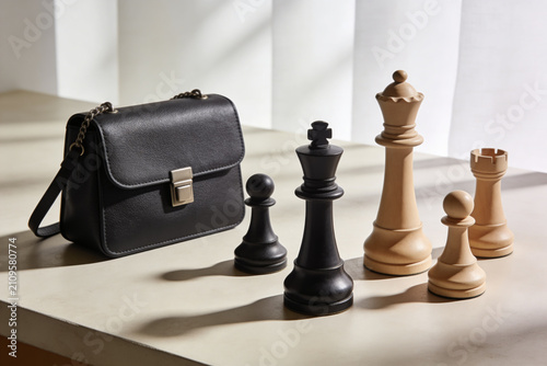 Bild auf Leinwand Stylish black handbag and classic chess pieces arranged on a neutral surface