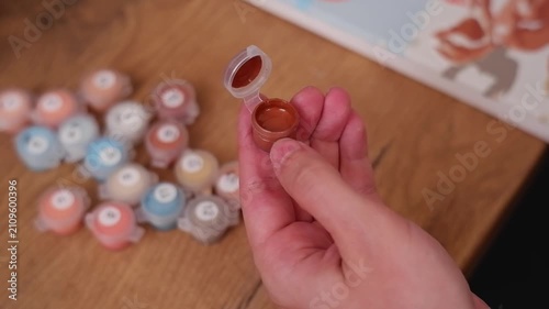 Close up of female hands dipping a brush into a small container of brown acrylic paint for a hobby