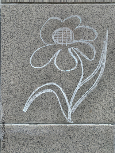 White chalk drawing of a flower on a grey stone pavement.