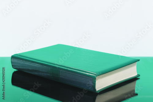 A closed green book on a red table on a white background with a copy space