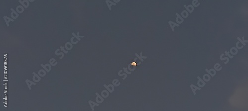 Bild auf Leinwand The pale sliver of the moon is visible against the deep blue of the evening sky,