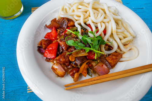 Kung pao, noodle and chopstick on white plate on blue background, closeup.