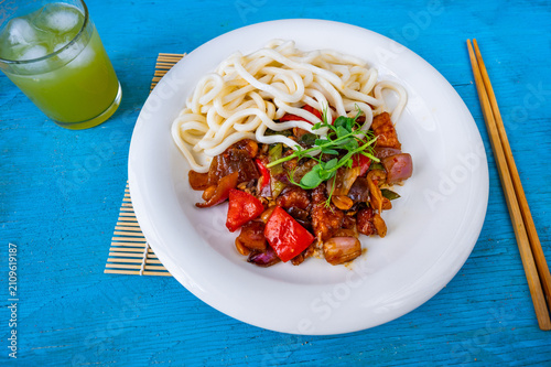 Fotografía Kung pao, noodle and chopstick on white plate on blue background, closeup