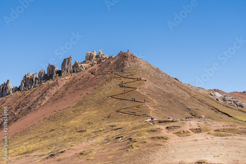 Bild auf Leinwand A group of hikers ascends a steep, zigzagging dirt trail leading to the summit r