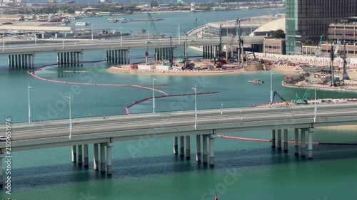 Modern coastal highway bridges and heavy construction machinery working on waterfront urban development project near turquoise ocean bay aerial sunny view