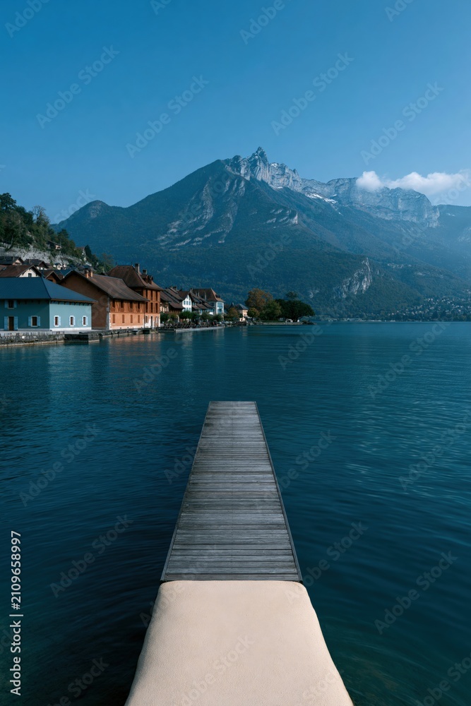 Fototapeta premium Centered wooden jetty leading into alpine lake with mountain skyline for minimalist wallpaper and poster design