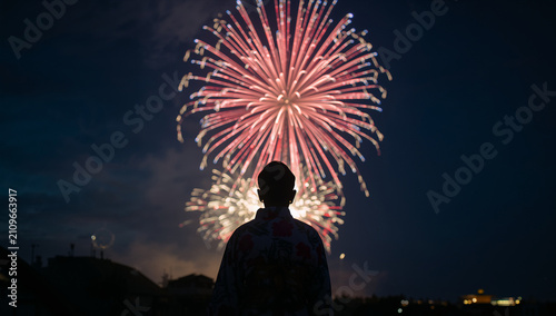 夏の夜空に大きく打ち上がる大輪の華やかな花火をあおぎ見る和装・浴衣姿の人物のシルエット