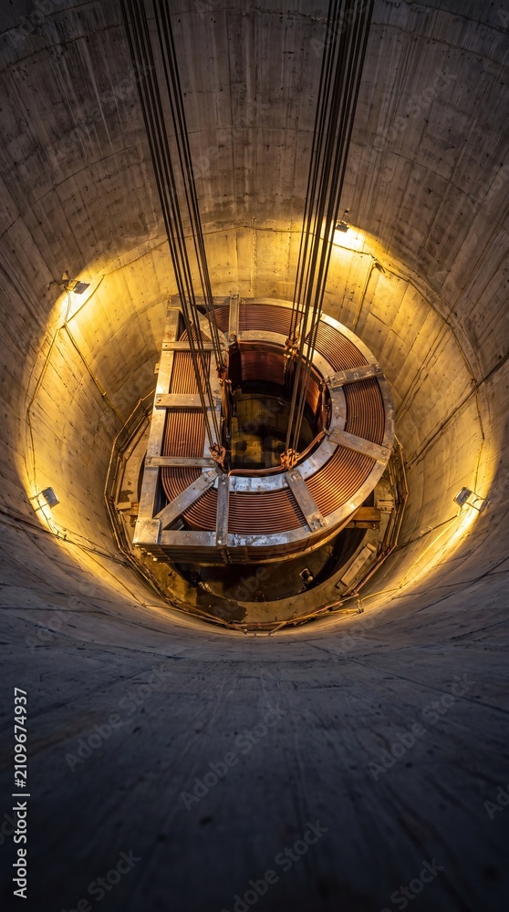 Fototapeta premium Large copper-wound electrical assembly suspended inside a deep industrial shaft.
