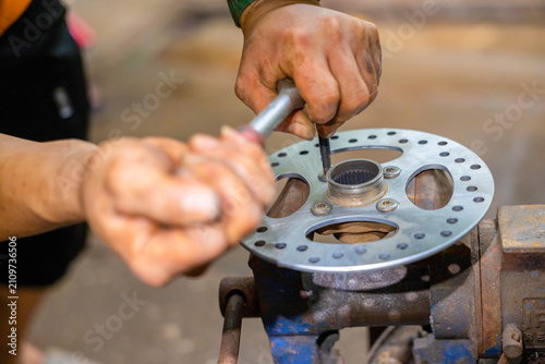 Foto Mechanic hand holding screwdriver while assembling metal brake rotor on rusty wo