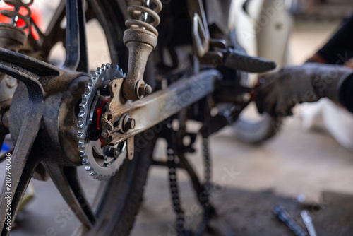 Fotografie Old motorcycle rear wheel and worn chain being repaired in dim workshop, mechani