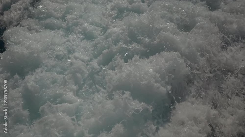 Turbulent white foam water trail behind a large boat in a calm blue sea on a sunny day, slow motion