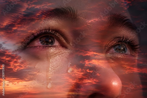 Emotional double exposure close-up portrait of crying eyes blending with a dramatic fiery sunset sky