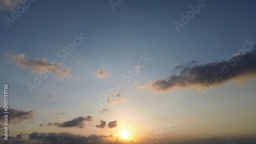 Beautiful sunset sky landscape with bright glowing sun and scattered clouds over distant mountains. Serene golden hour nature background.
