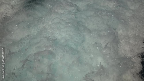 Turbulent white foam water trail behind a large boat in a calm blue sea on a sunny day, slow motion