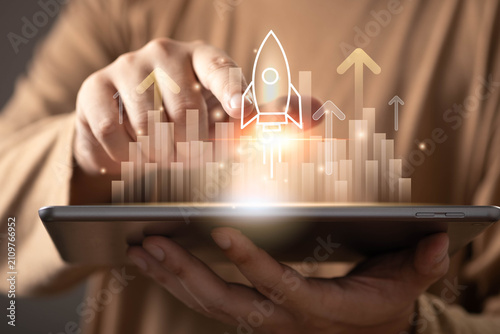 Obraz na plátne Business growth and startup launch concept featuring a rocket taking off from a digital platform with rising charts and upward arrows, symbolizing innovation, investment success, business development